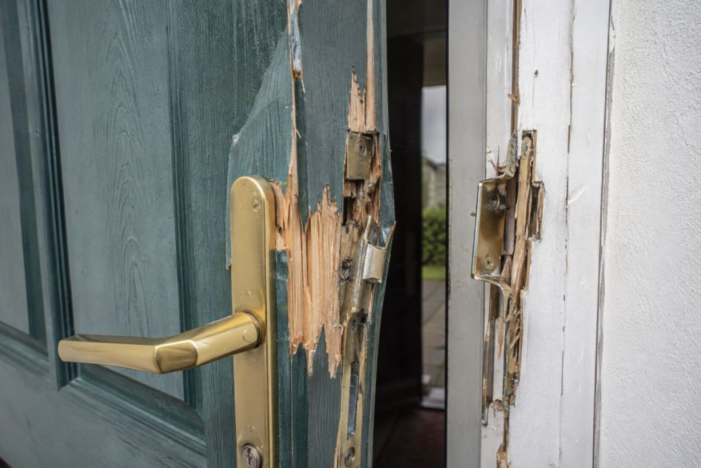 Forced domestic front door with splintered timber and a torn strike plate after a break-in