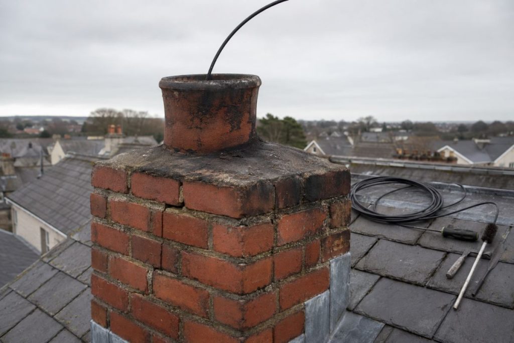 Flue inspection camera fed into a soot-stained chimney pot during a chimney fire claim survey