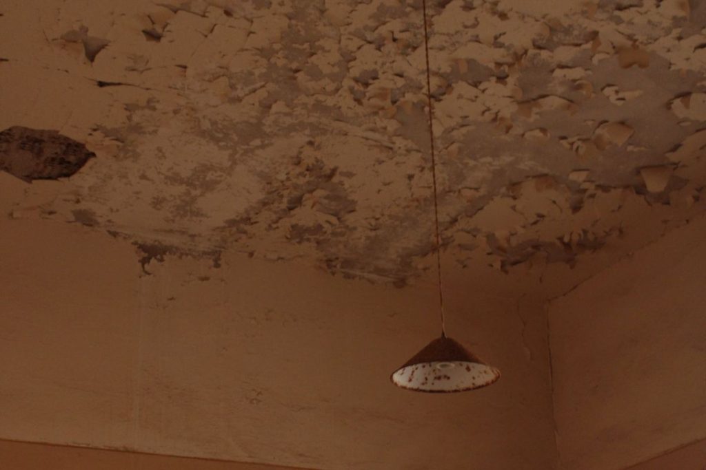 Water-damaged ceiling with blown plaster and damp staining caused by an escape of water from pipework above