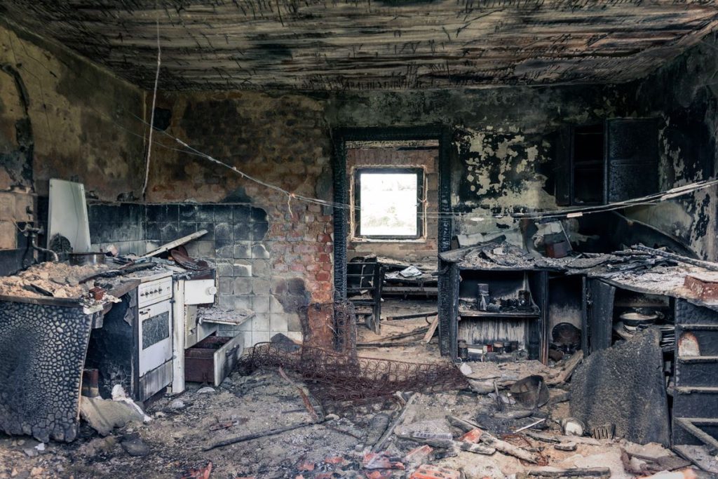 Fire and smoke damaged kitchen with charred walls and soot-covered fittings
